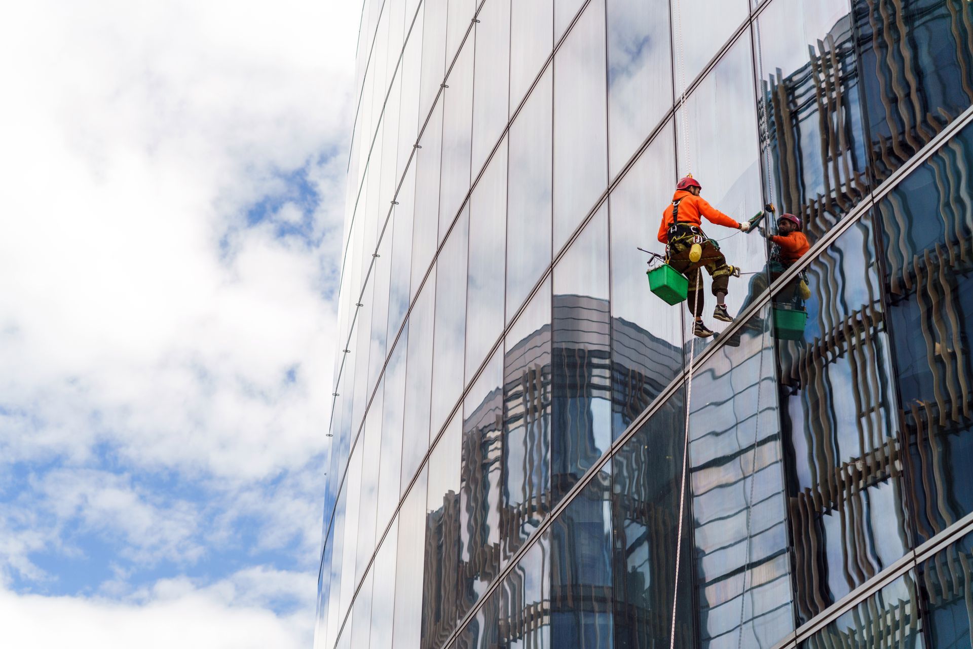 Window washers on a high-rise building with reflective glass, cleaning the exterior. Sky with clouds.