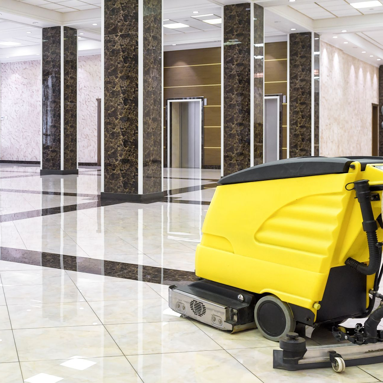 Yellow floor cleaner in a polished marble-floored lobby, cleaning.  Columns and elevators in the background.