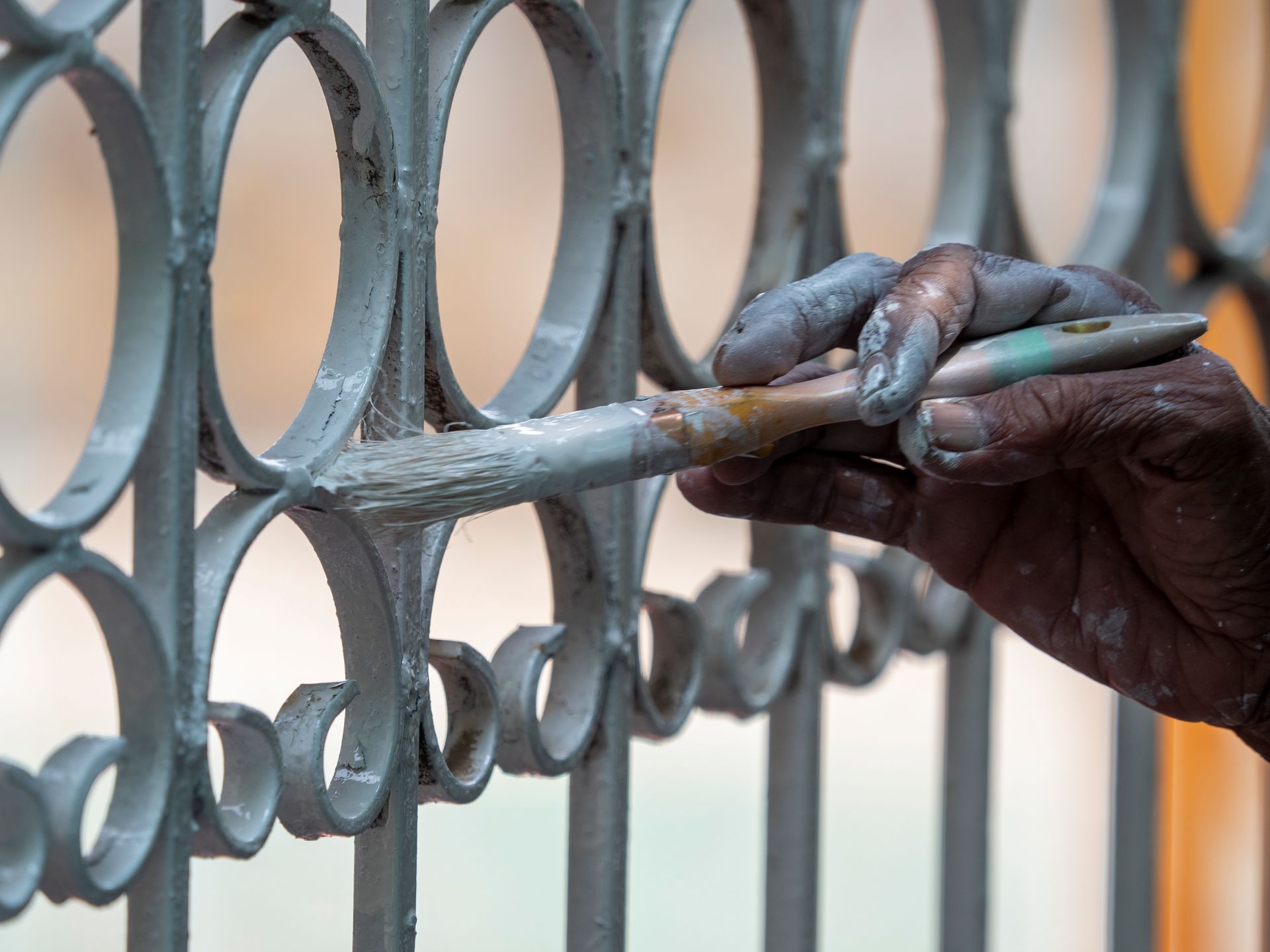 A person's hand painting a gray metal gate with a brush, outdoors.