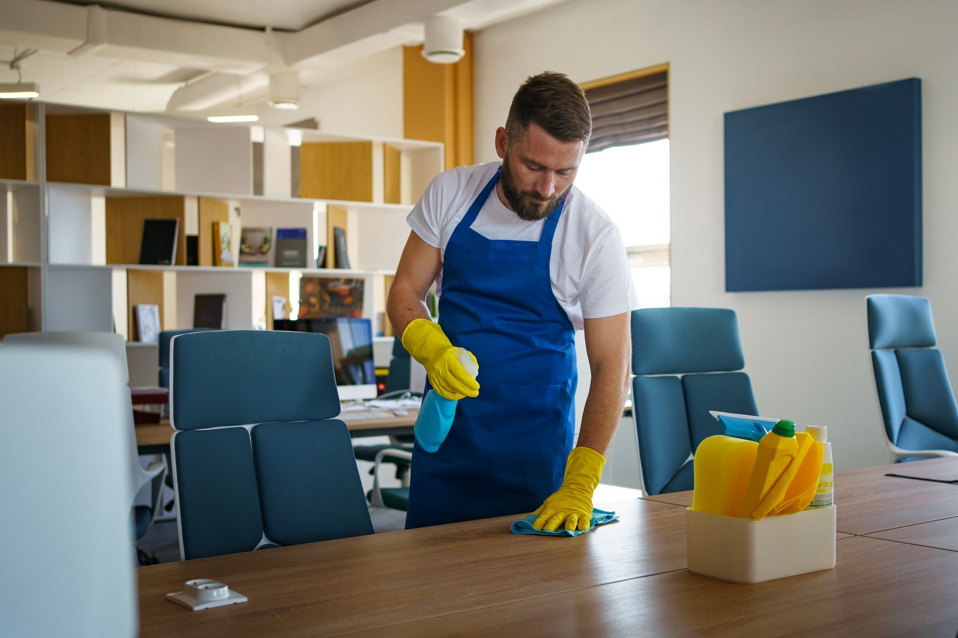 a man is cleaning a table in an office with a spray bottle .