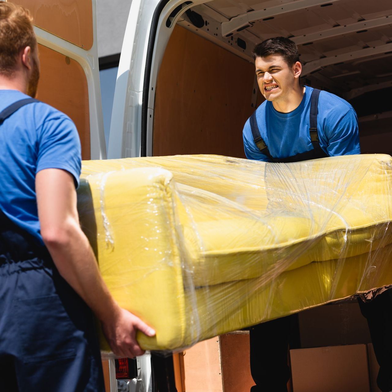 Two men are carrying a yellow couch out of a van.