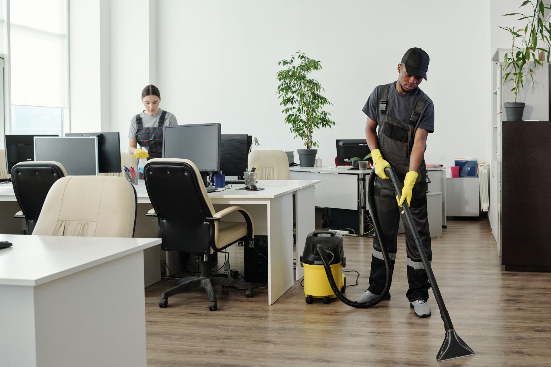 a man and a woman are cleaning an office with a vacuum cleaner .