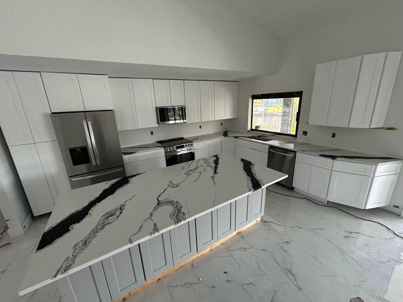 Modern white kitchen with black-veined marble island, stainless appliances, and large window