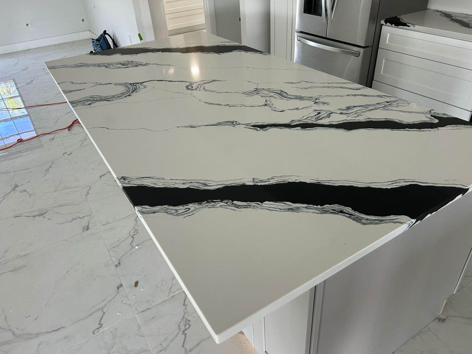 White marble-look kitchen island with a black veined countertop and visible damage along the front edge.