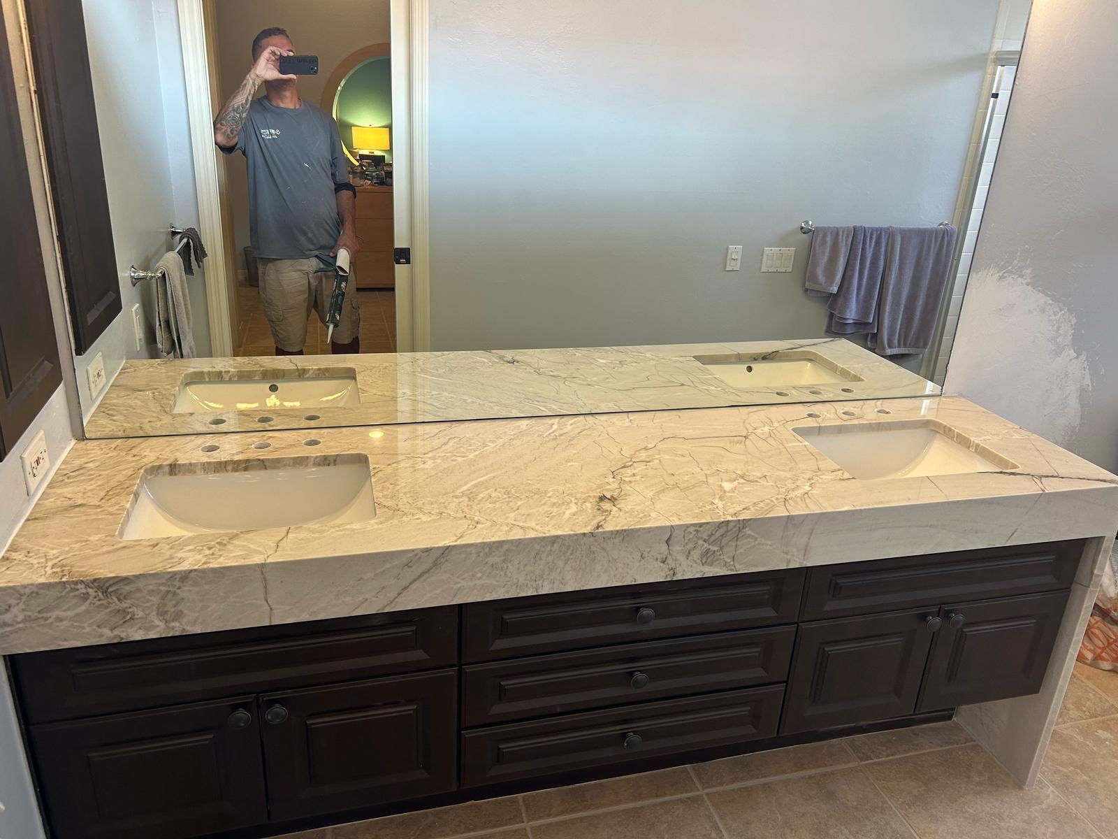 Bathroom vanity with double sinks, large mirror, and person taking a mirror selfie in the background.