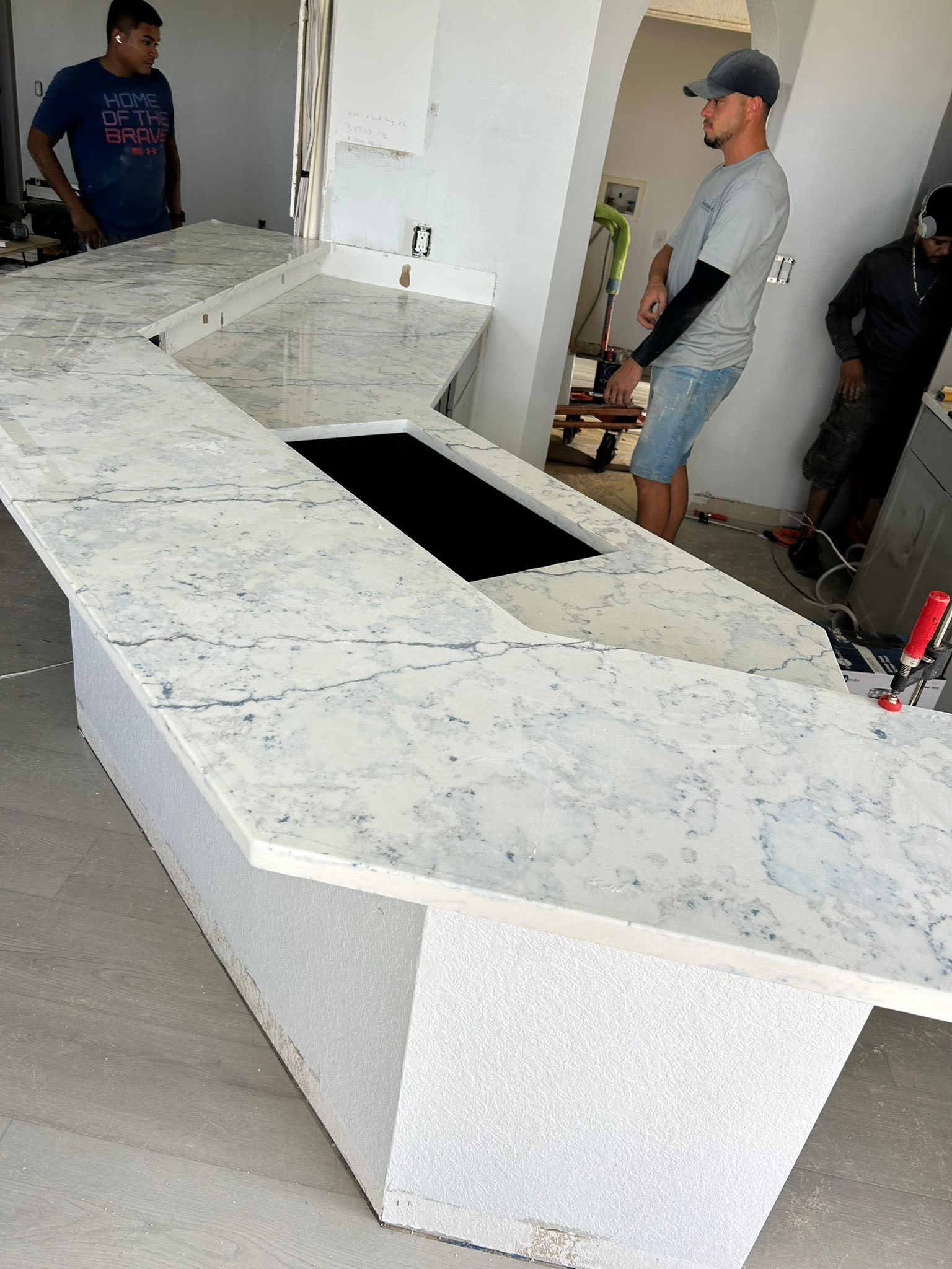 Large white speckled stone countertop being installed in a room, with workers nearby