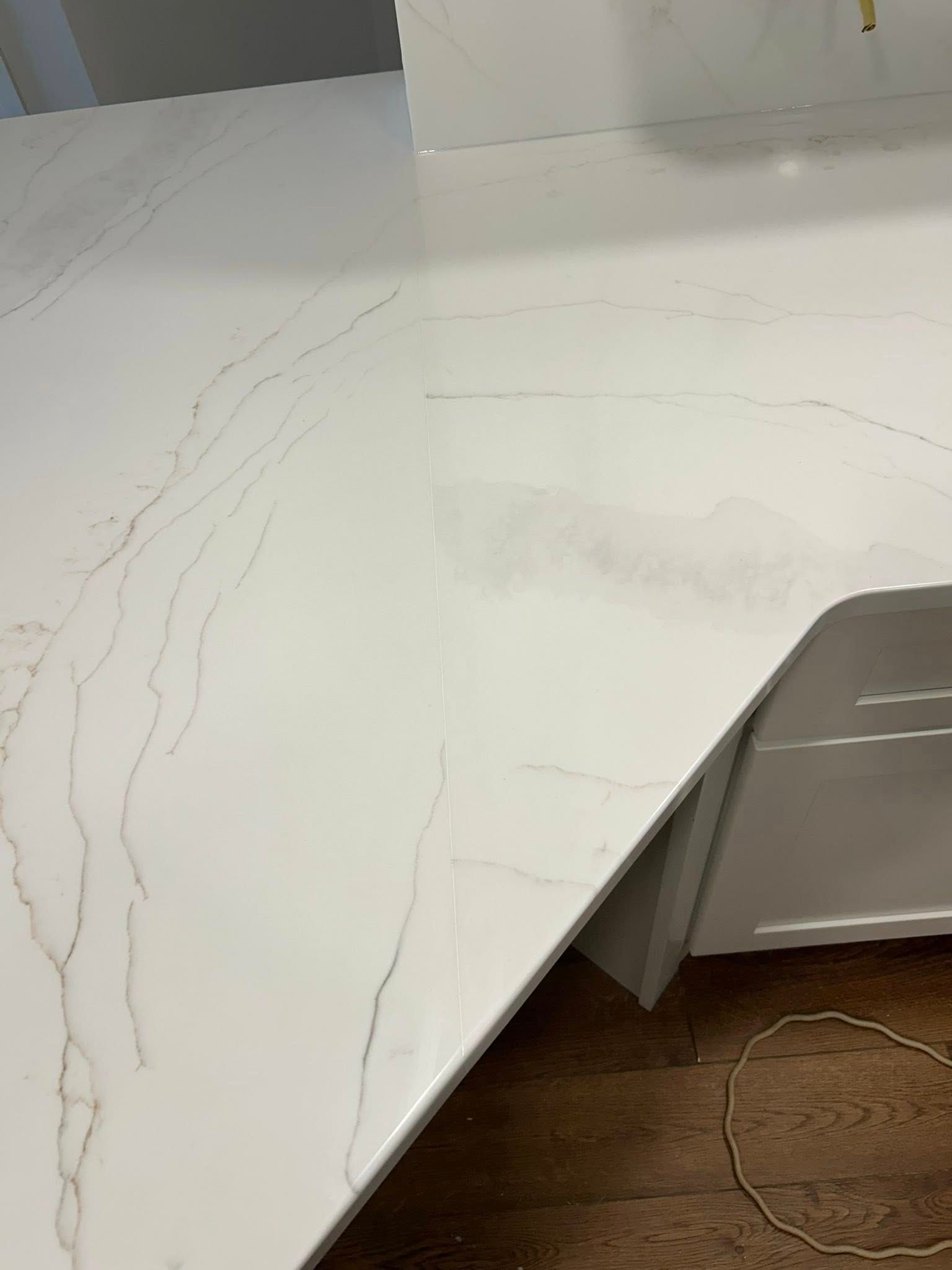 White marble-look countertop with visible cracks and a damaged corner over a wood floor.