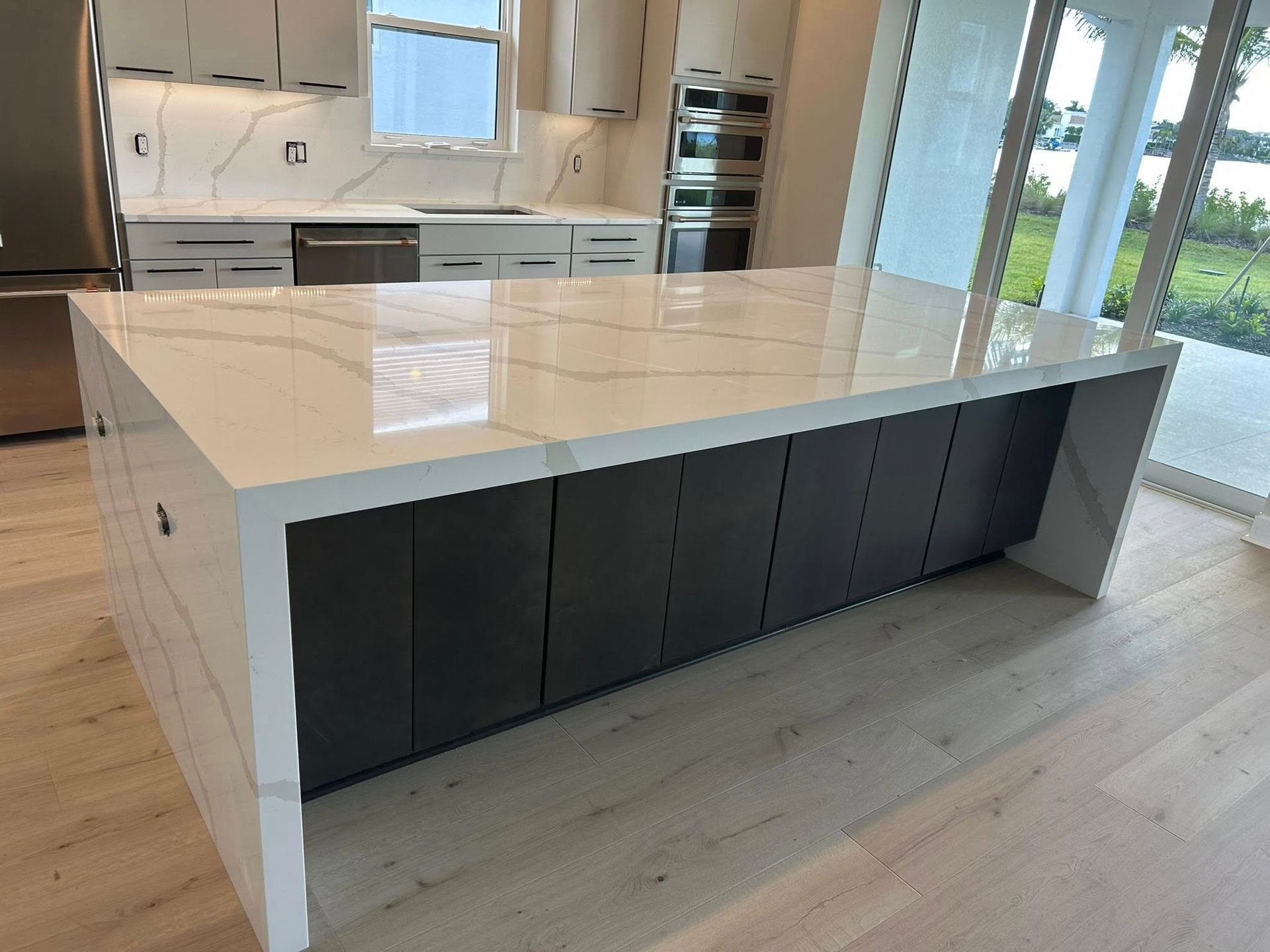 Modern kitchen island with white marble top and dark cabinet fronts in a bright, open kitchen