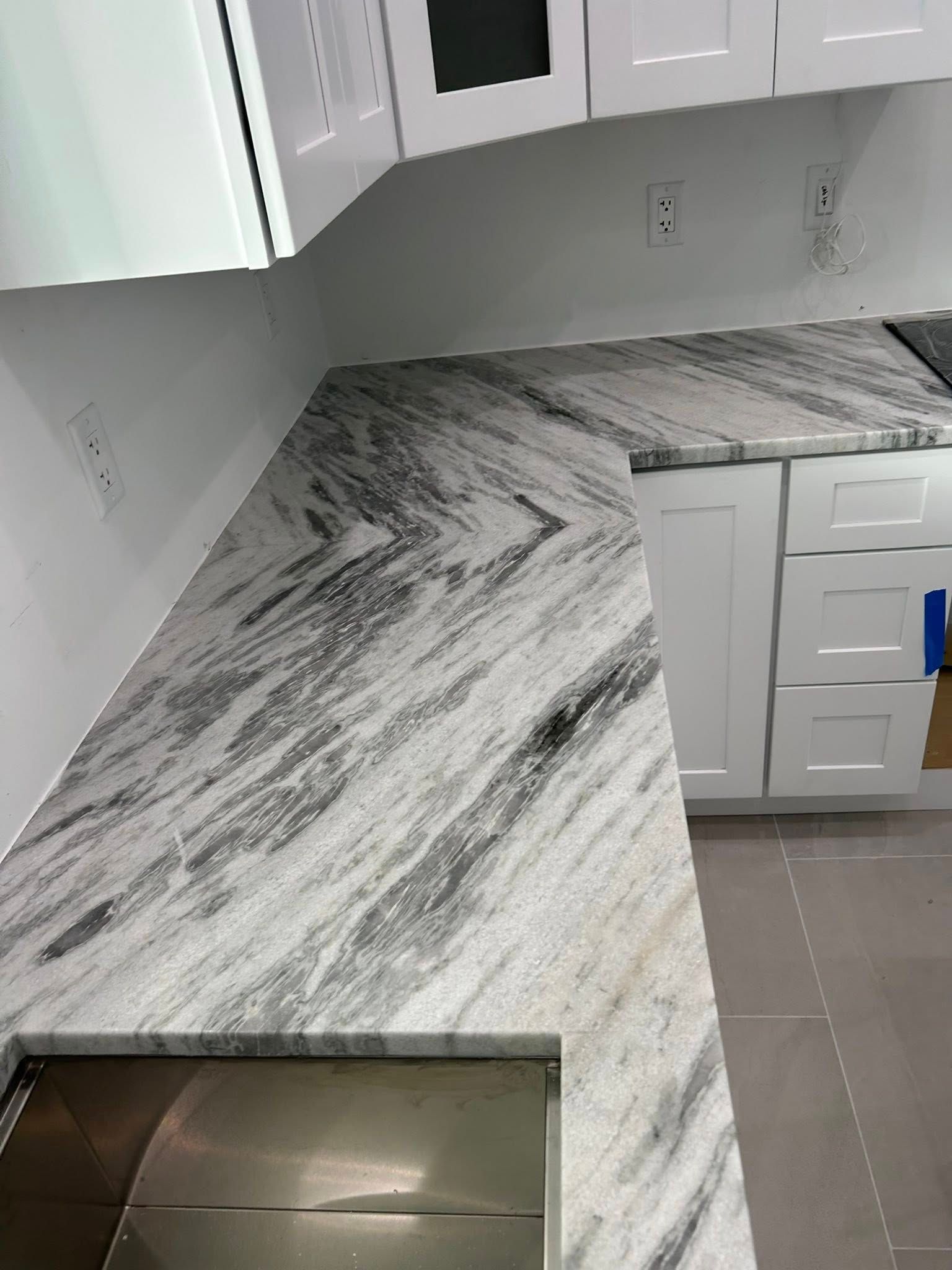 Modern kitchen with white cabinets and gray marble-pattern countertops, including a corner sink.