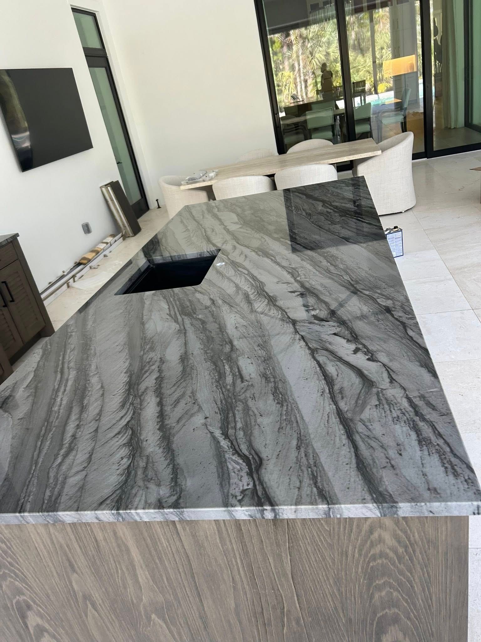 Modern kitchen with a gray marble island, white cabinets, and a view into a bright living area.