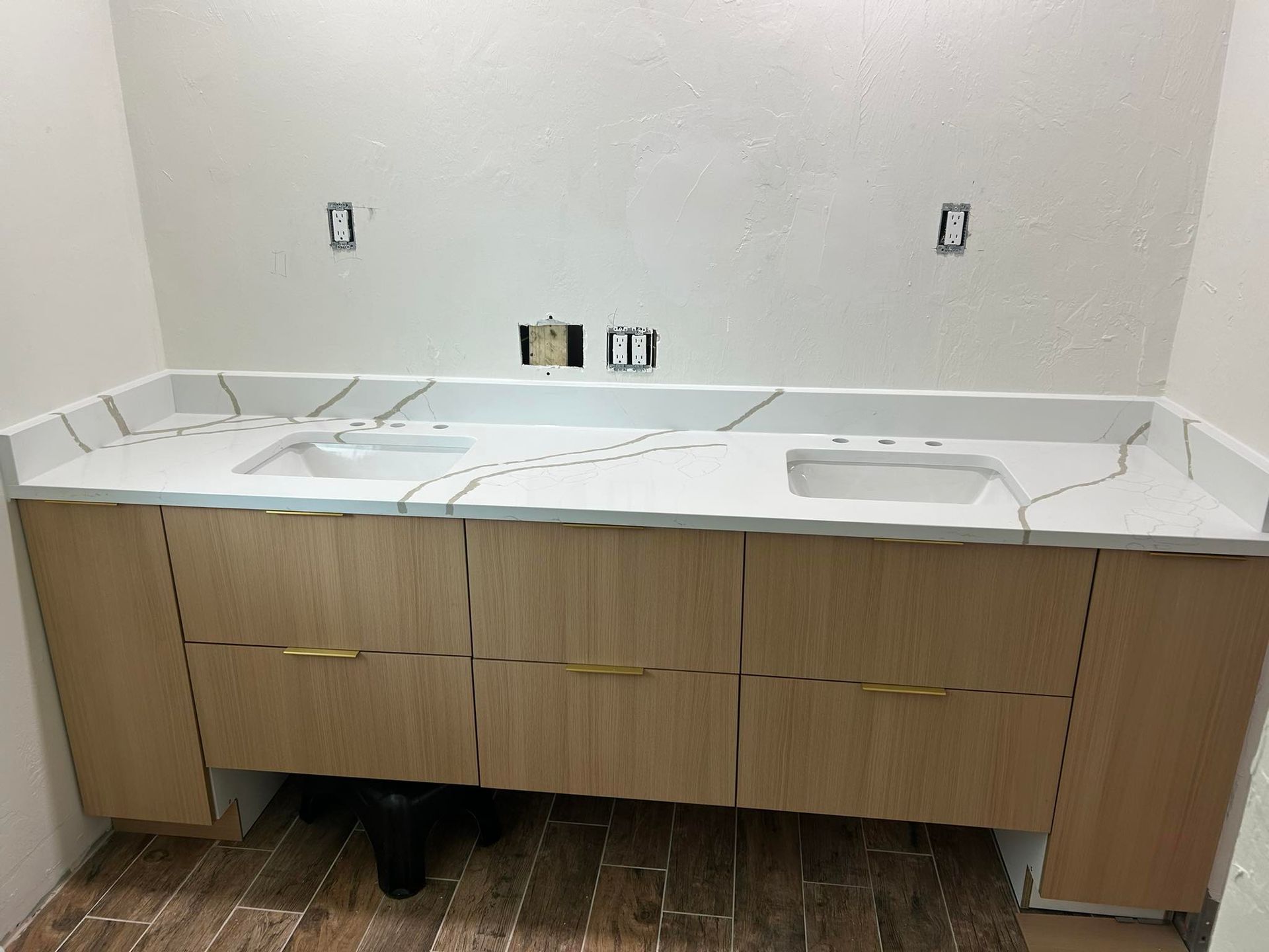 Unfinished bathroom vanity with white countertop, wood cabinets, and exposed plumbing under the sink.