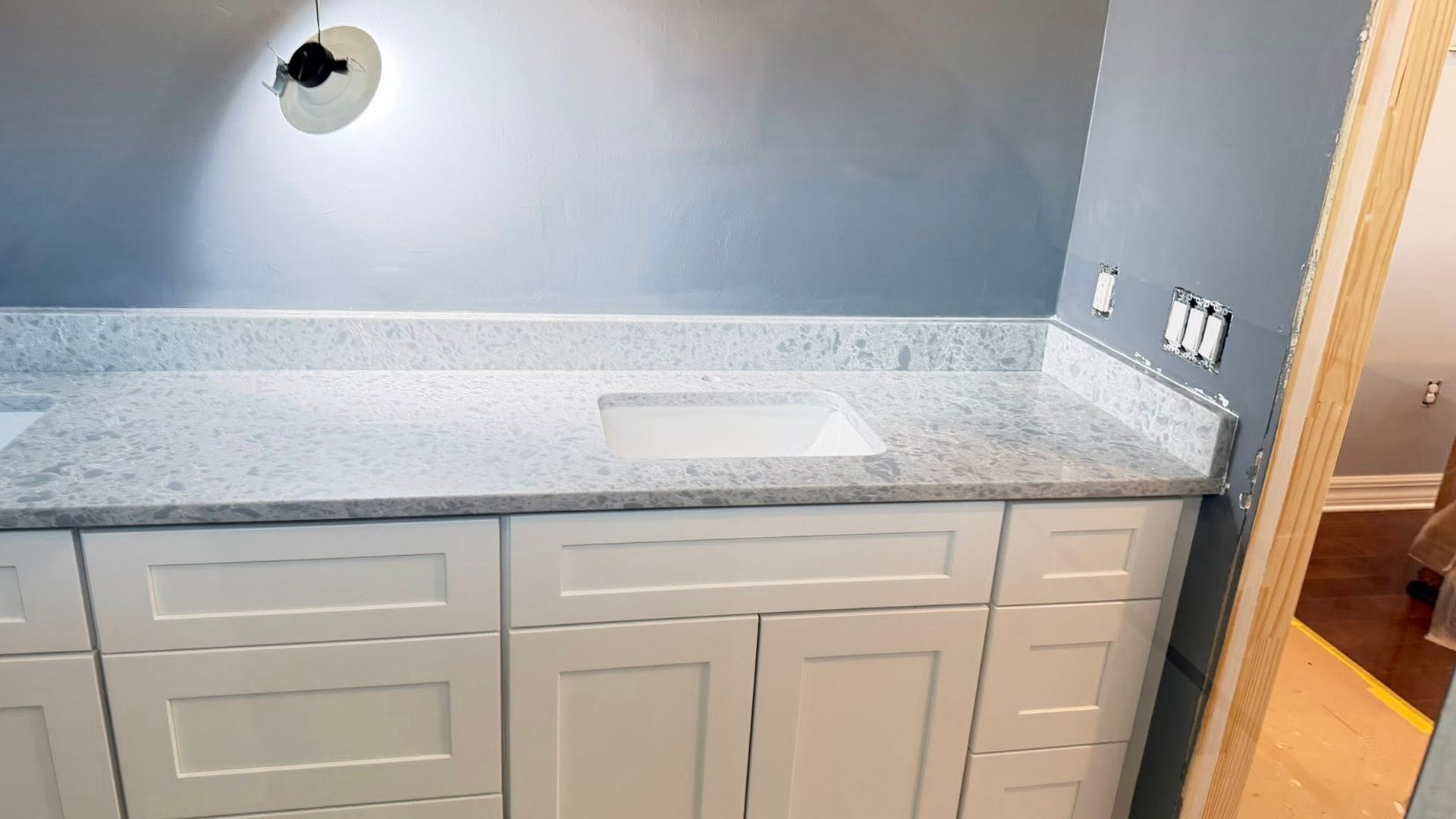 Gray bathroom vanity with white countertop, sink, and wall light under a slanted ceiling