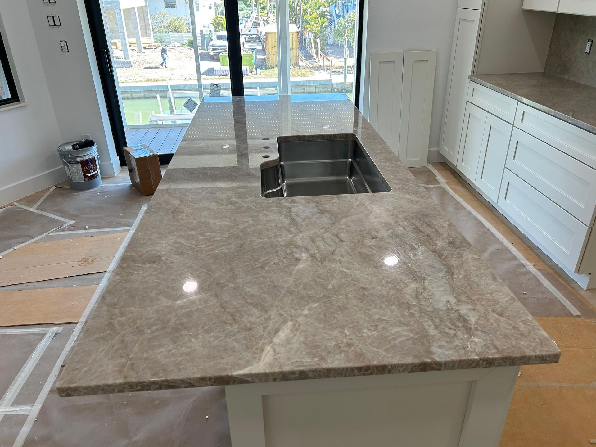 Modern kitchen island with marble countertop, sink, and light wood cabinetry near large sliding glass doors