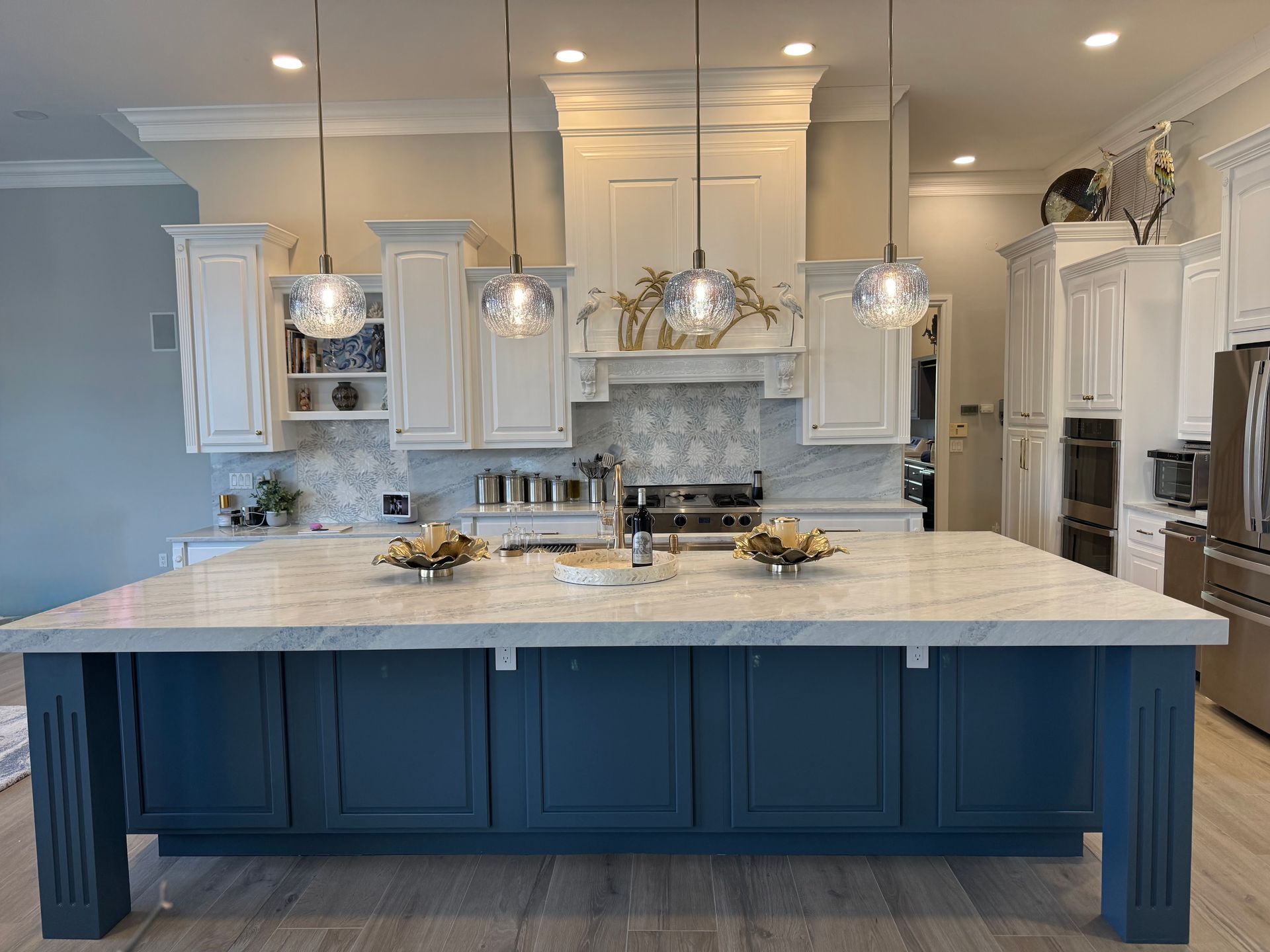 Modern kitchen with white cabinets, marble island, and blue island base lit by pendant lights