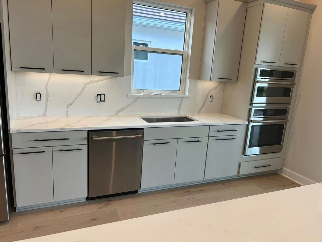 Modern white kitchen with gray cabinets, stainless appliances, and a window above the sink.