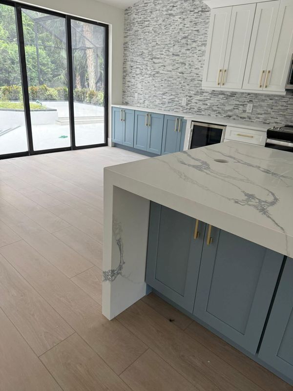 Modern kitchen with blue cabinets, marble island, and sliding glass doors to a patio.