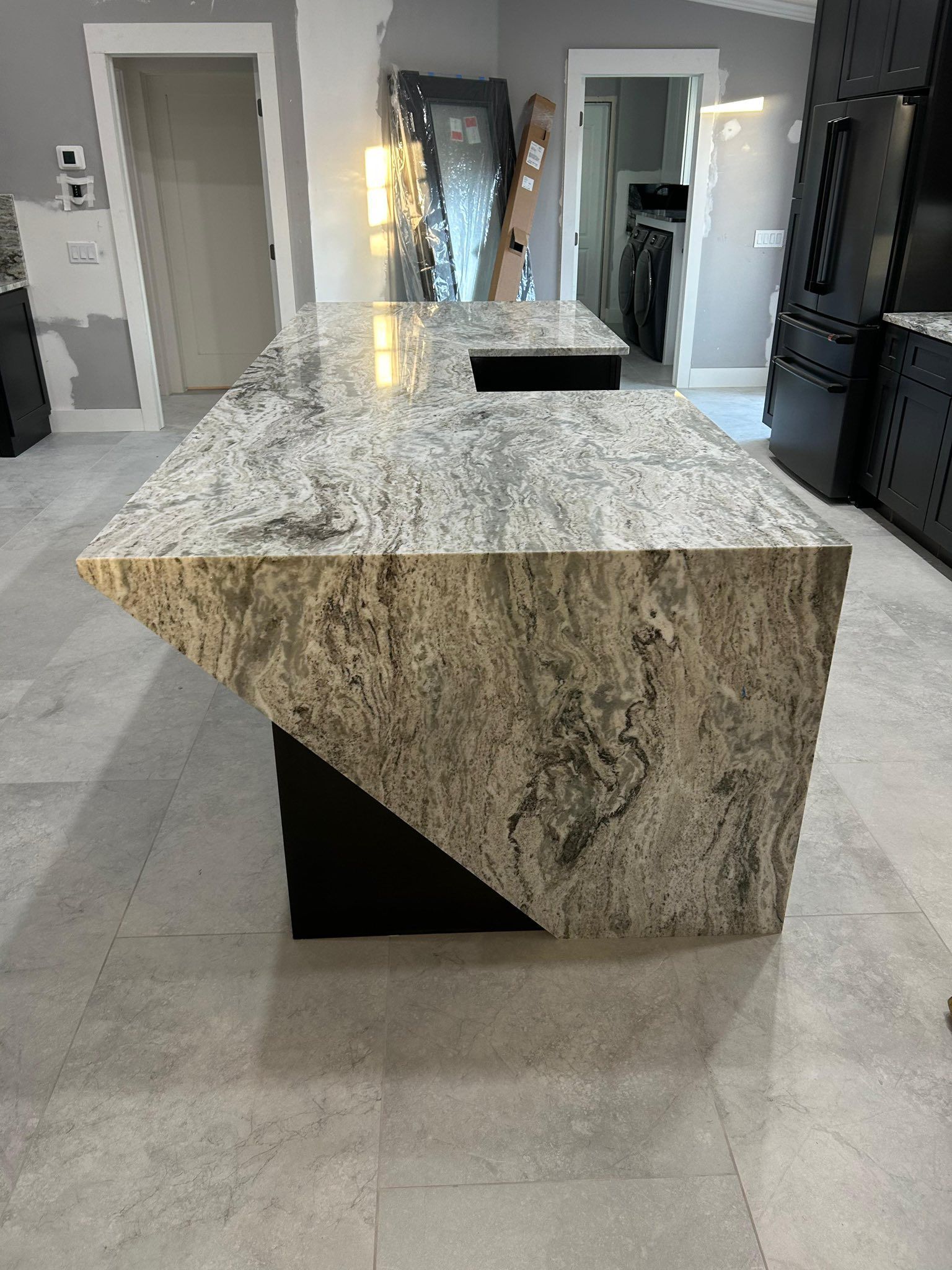 Large speckled granite kitchen island in a modern home, with gray tile floors and open doorways.