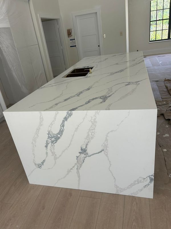White marble-look kitchen island in a bright unfinished room with light wood flooring.
