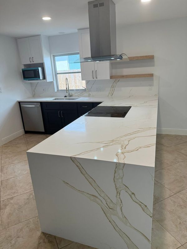 Modern kitchen with white marble island, stainless steel appliances, and dark wood flooring