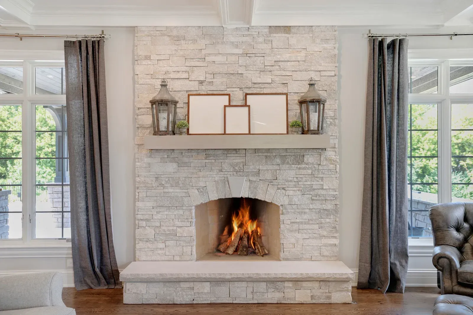 Rustic stone fireplace with a small fire, brass tools, and a wooden chair nearby.