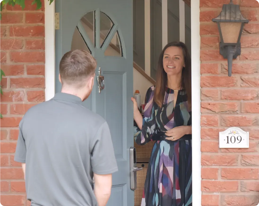 Woman smiles while opening a door for a person, brick exterior. Door marked '109'.