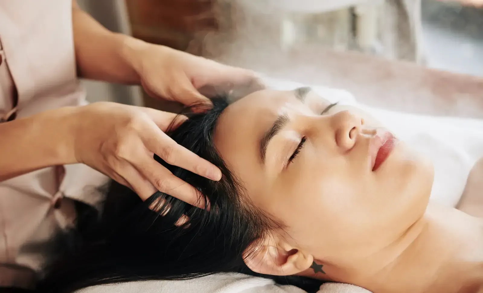 Woman getting a head massage with eyes closed, outdoors. Hands massaging head.