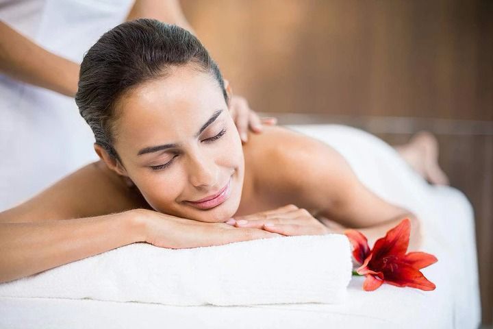 Woman receiving back massage at spa, smiling, with red flower.