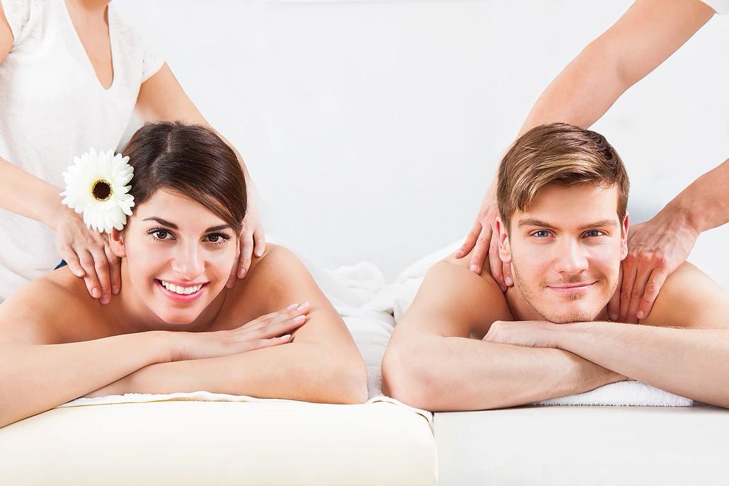 Couple getting massages, smiling. White room setting, massage therapists.