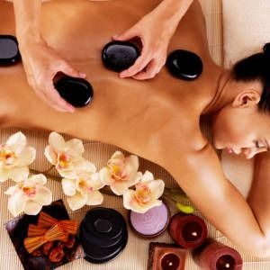 Woman receiving a hot stone massage, with flowers and candles arranged on a wooden surface.
