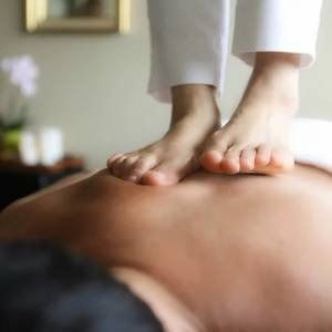 Feet on someone's back during Thai massage. White pants. Indoors.