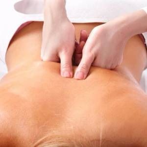Hands massaging a person's lower back, likely in a spa setting. Focus on skin, touch, and care.