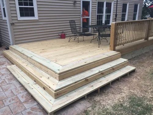 A wooden deck with stairs and a table and chairs on it in front of a house.