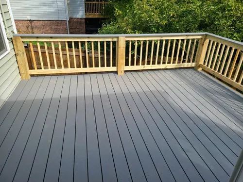 A gray deck with a wooden railing and a house in the background