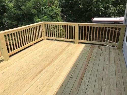 A wooden deck with a railing and trees in the background.