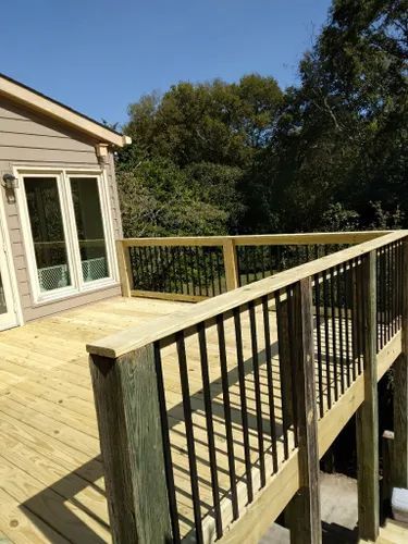 A wooden deck with a metal railing is in front of a house.