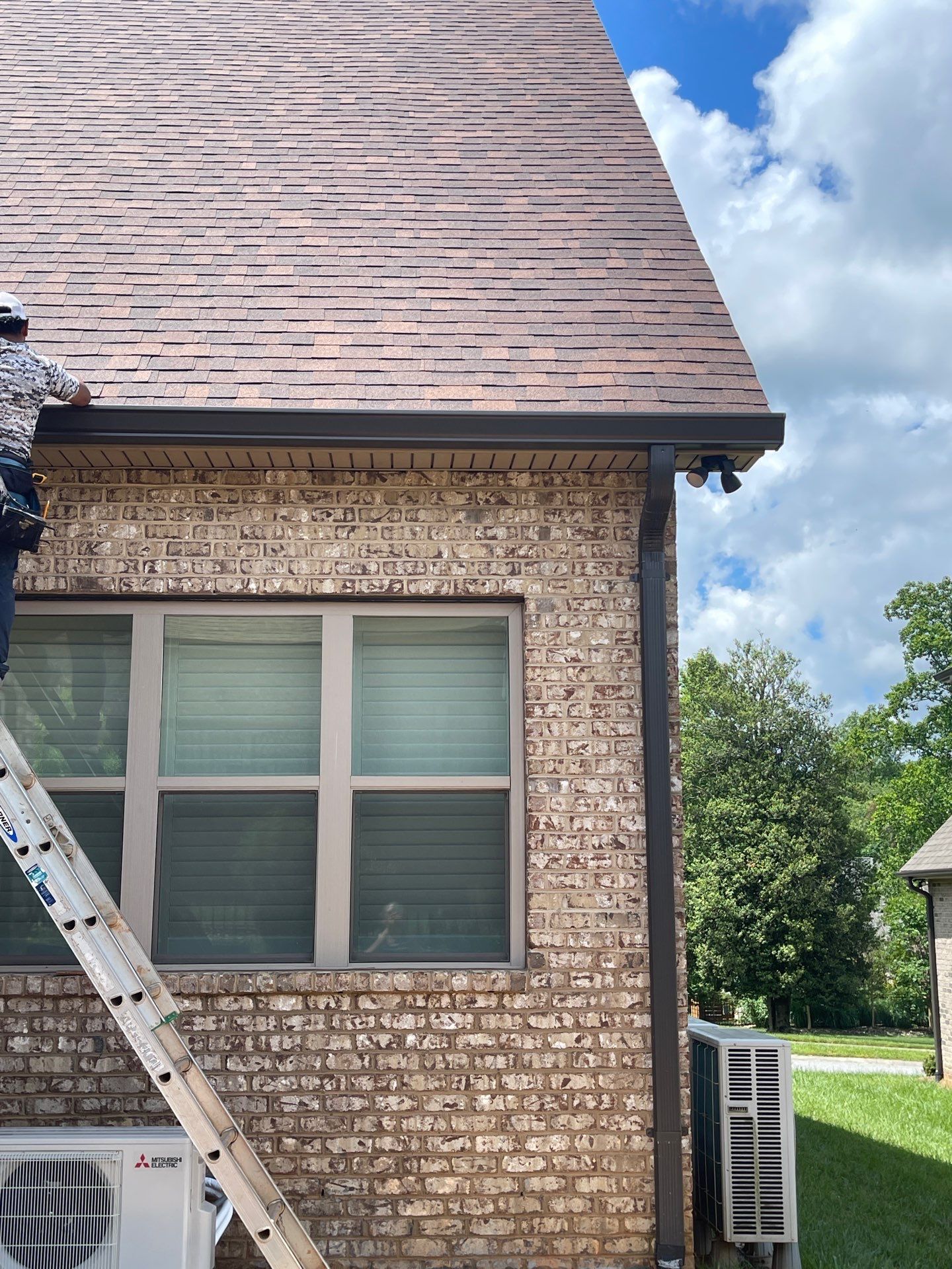 A man is standing on a ladder on the side of a brick house.