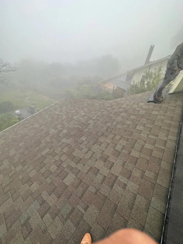 A person is standing on top of a roof in the fog.