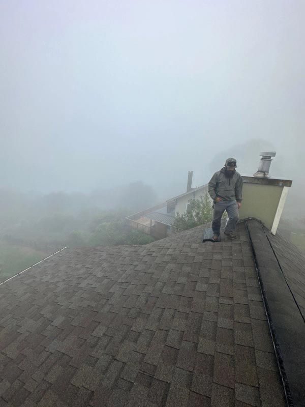 A man is standing on top of a roof in the fog.