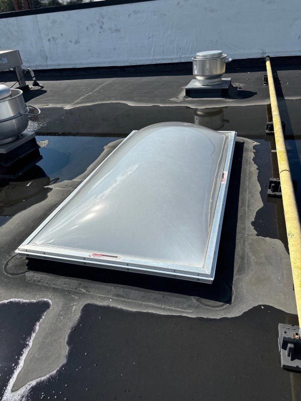 A skylight is sitting on top of a roof next to a measuring tape.