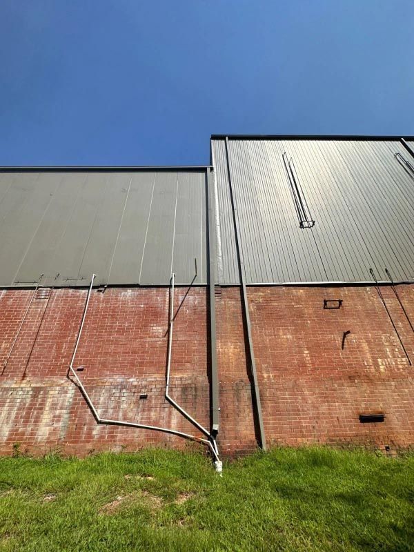 A brick building with a gray roof and a lot of pipes coming out of it.