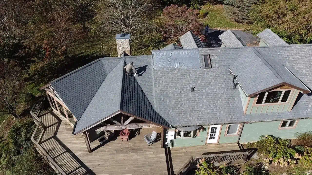 An aerial view of a large house with a gray roof surrounded by trees.