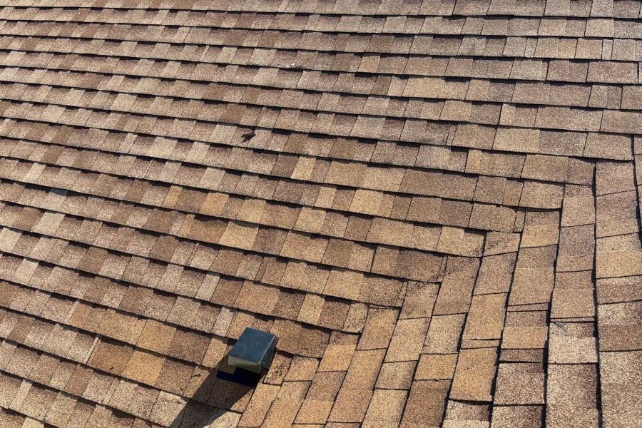 A close up of a roof with shingles and a vent on it.