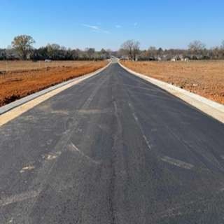 A newly paved road is going through a field.