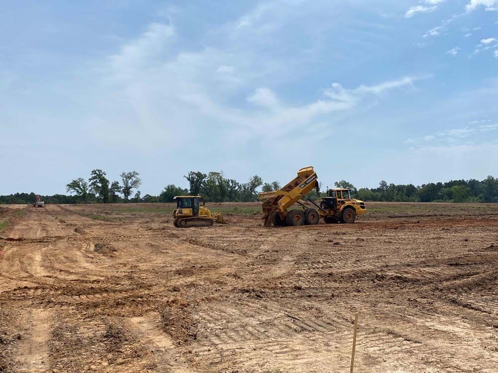 A bulldozer and a dump truck are driving through a dirt field.