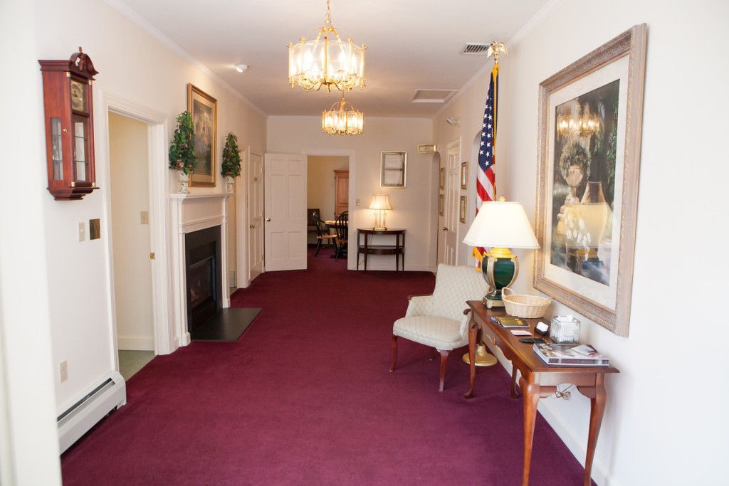 Long hallway with burgundy carpet, chandeliers, and a framed portrait, possibly a funeral home.