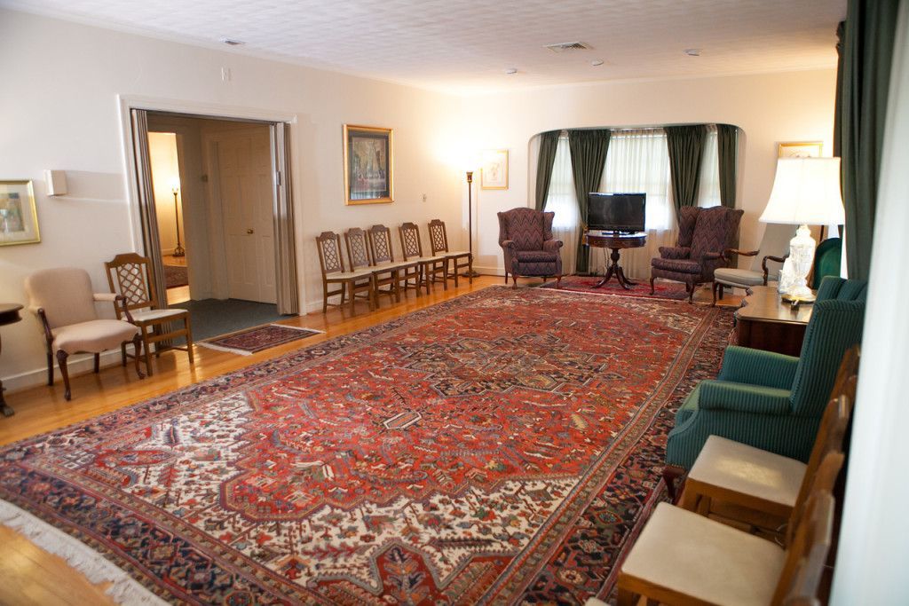 A long, ornate rug in a funeral home waiting room with chairs and a small TV.