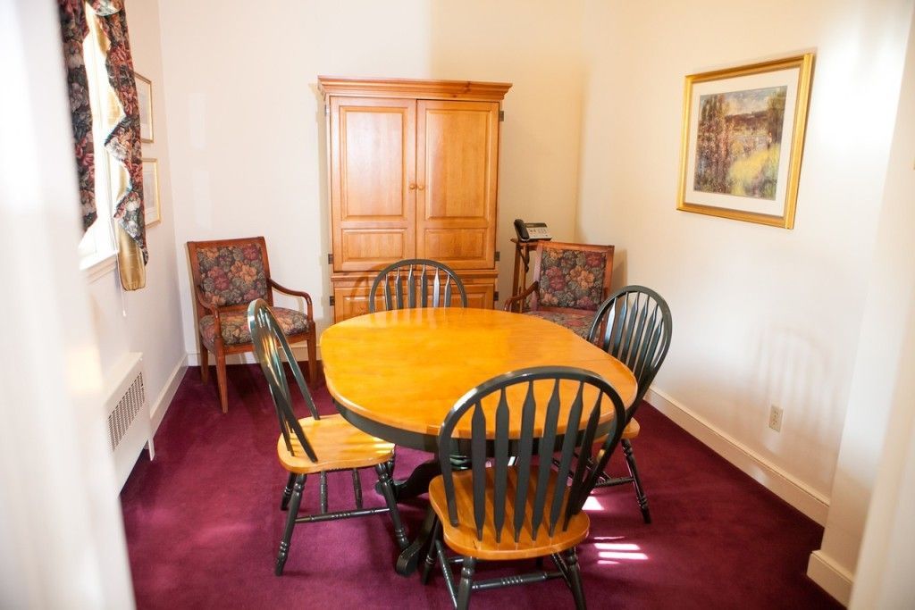 Dining room with wooden table and chairs, wooden cabinet, burgundy carpet, and artwork.