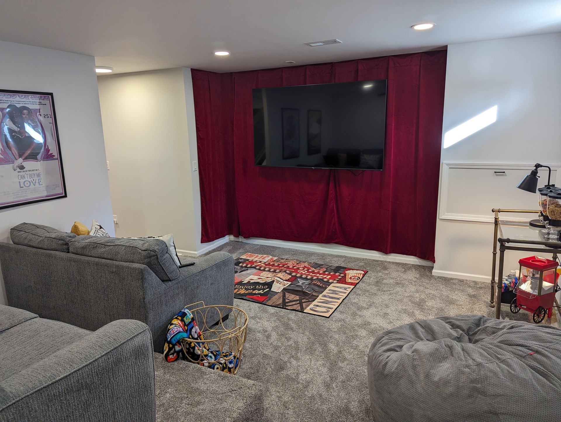 Cozy media room with a large TV on a burgundy curtain, gray couches, and a shaggy rug.