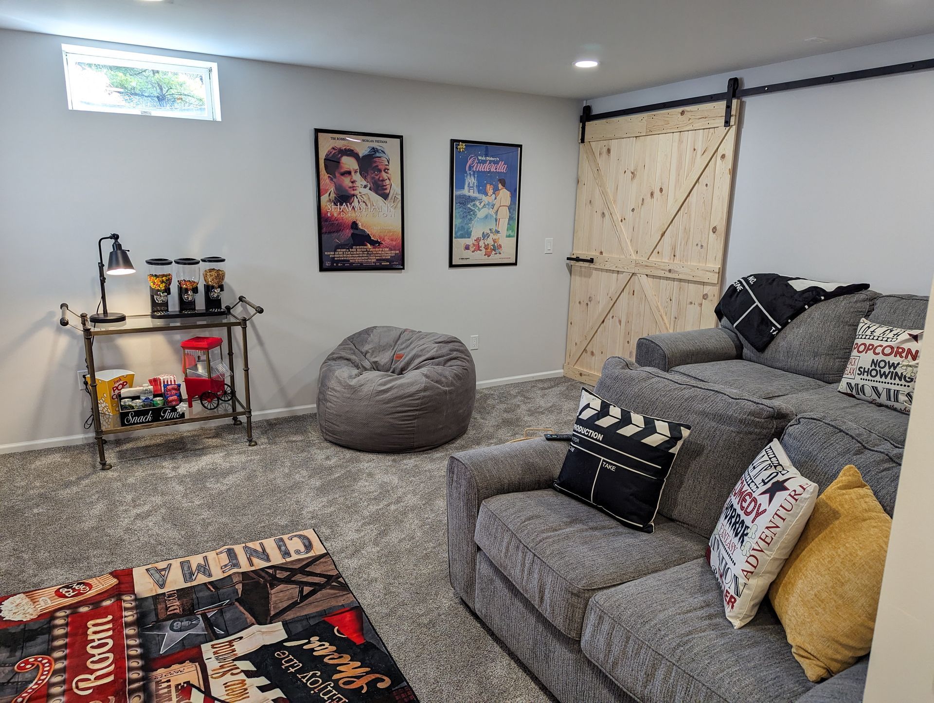 Cozy home theater: Gray sofa, beanbag, popcorn stand, movie posters, rug, and a wooden sliding door.