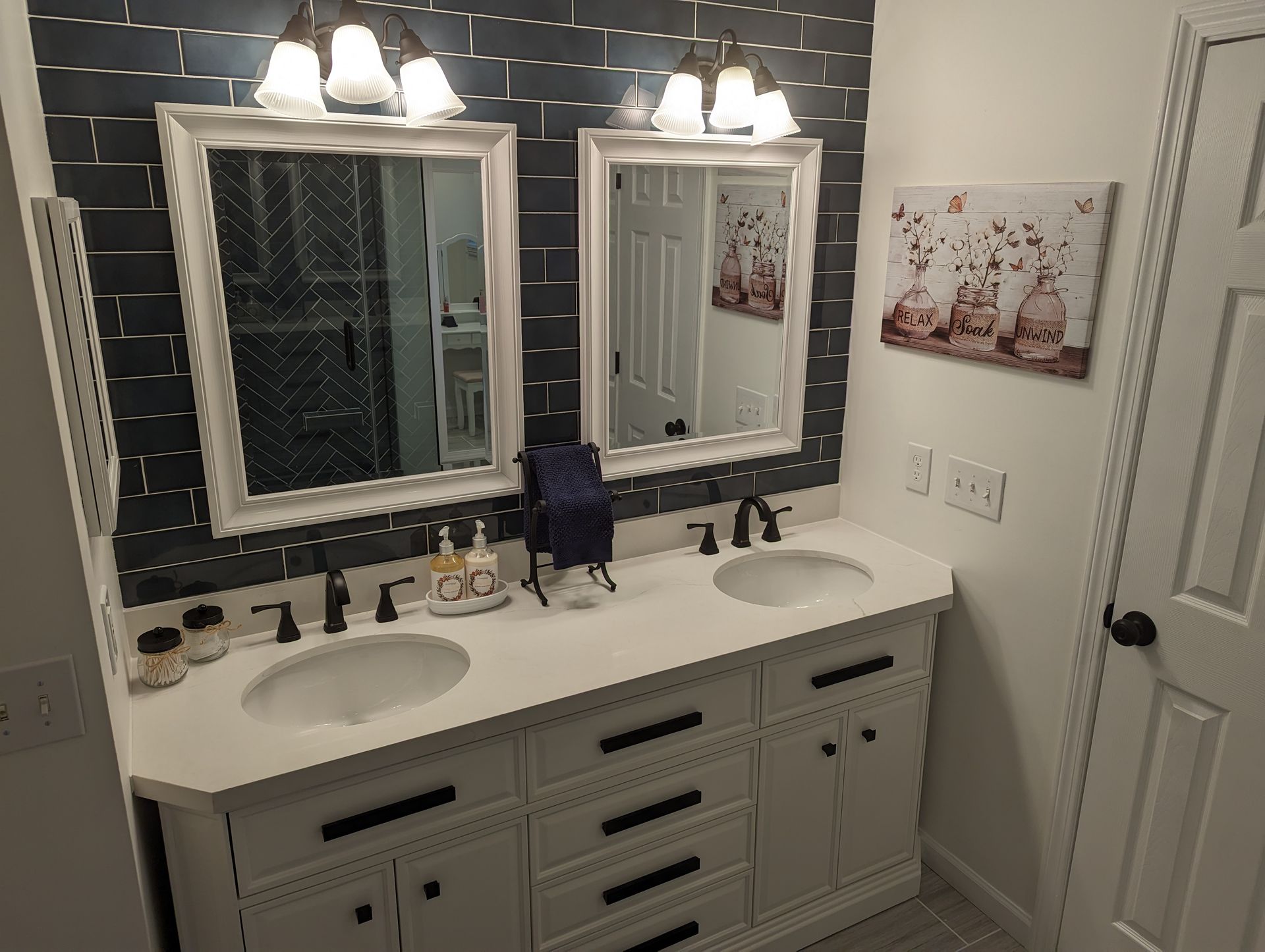 Bathroom with white double vanity, mirrors, black accents, and brick wall.
